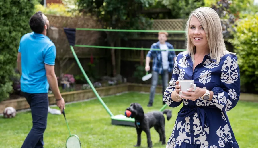 Laura stands in her garden with her family playing badminton in the background.